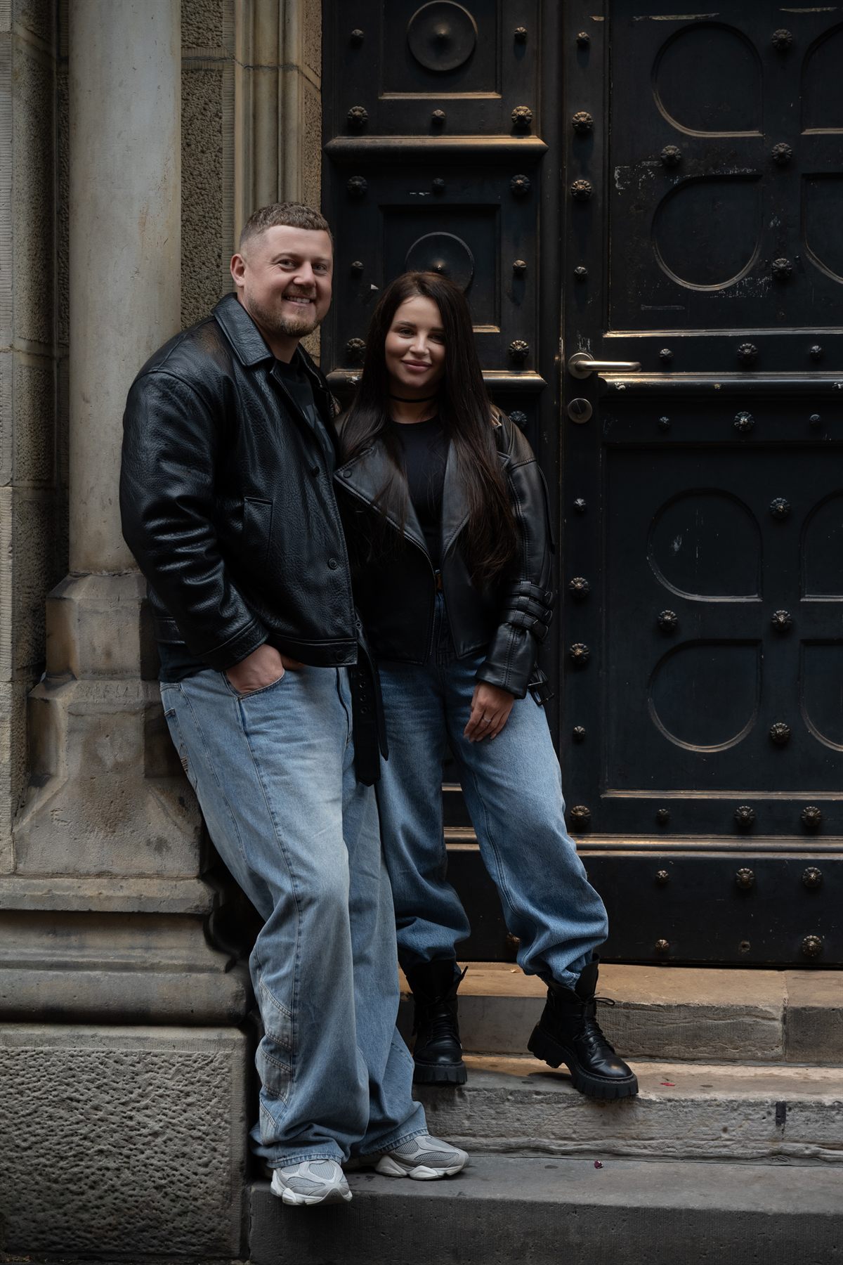 A couple in leather jackets standing on the steps of an old doorway