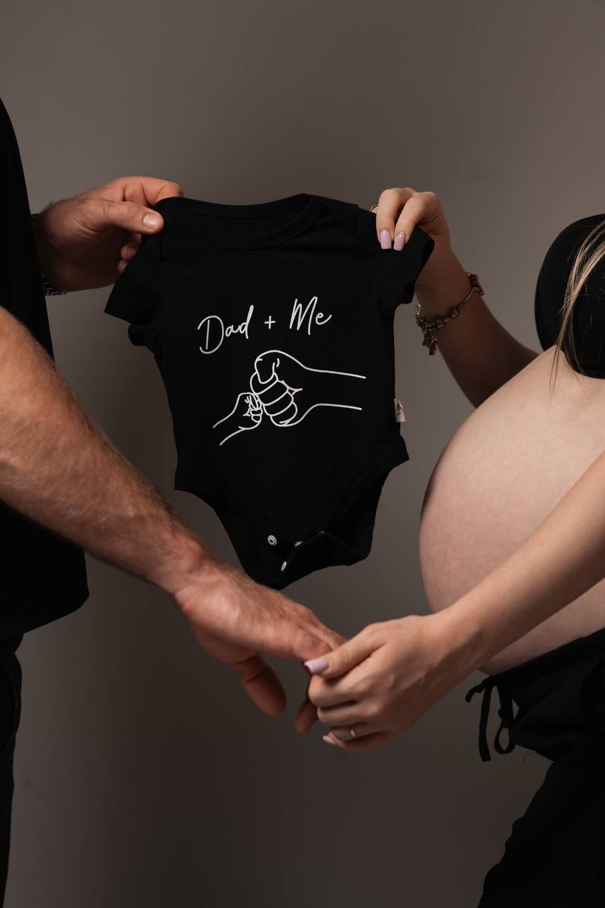 Expecting parents holding up a tiny black babygrow together