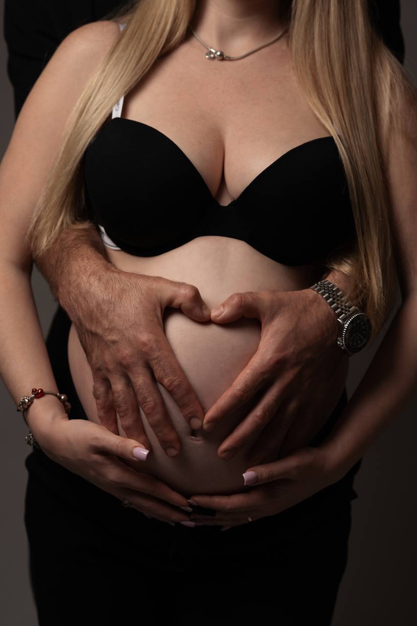 Two pairs of hands forming a heart on a pregnant belly
