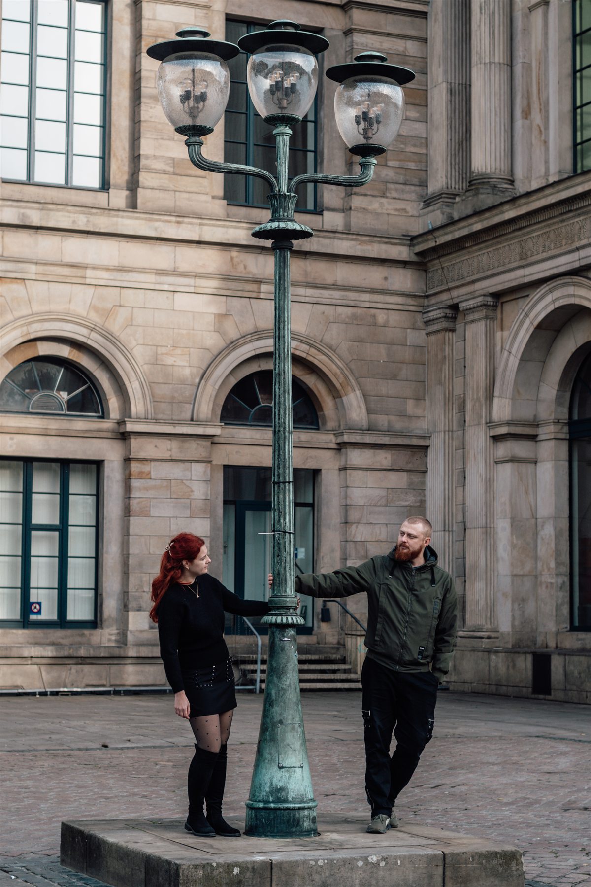 A couple either side of an old street lamp on a city square