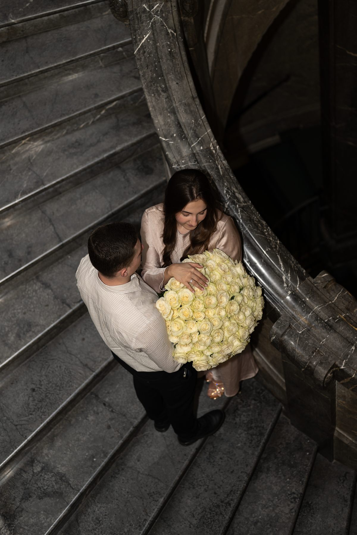 A couple on a spiral staircase with an armful of white roses, seen from above