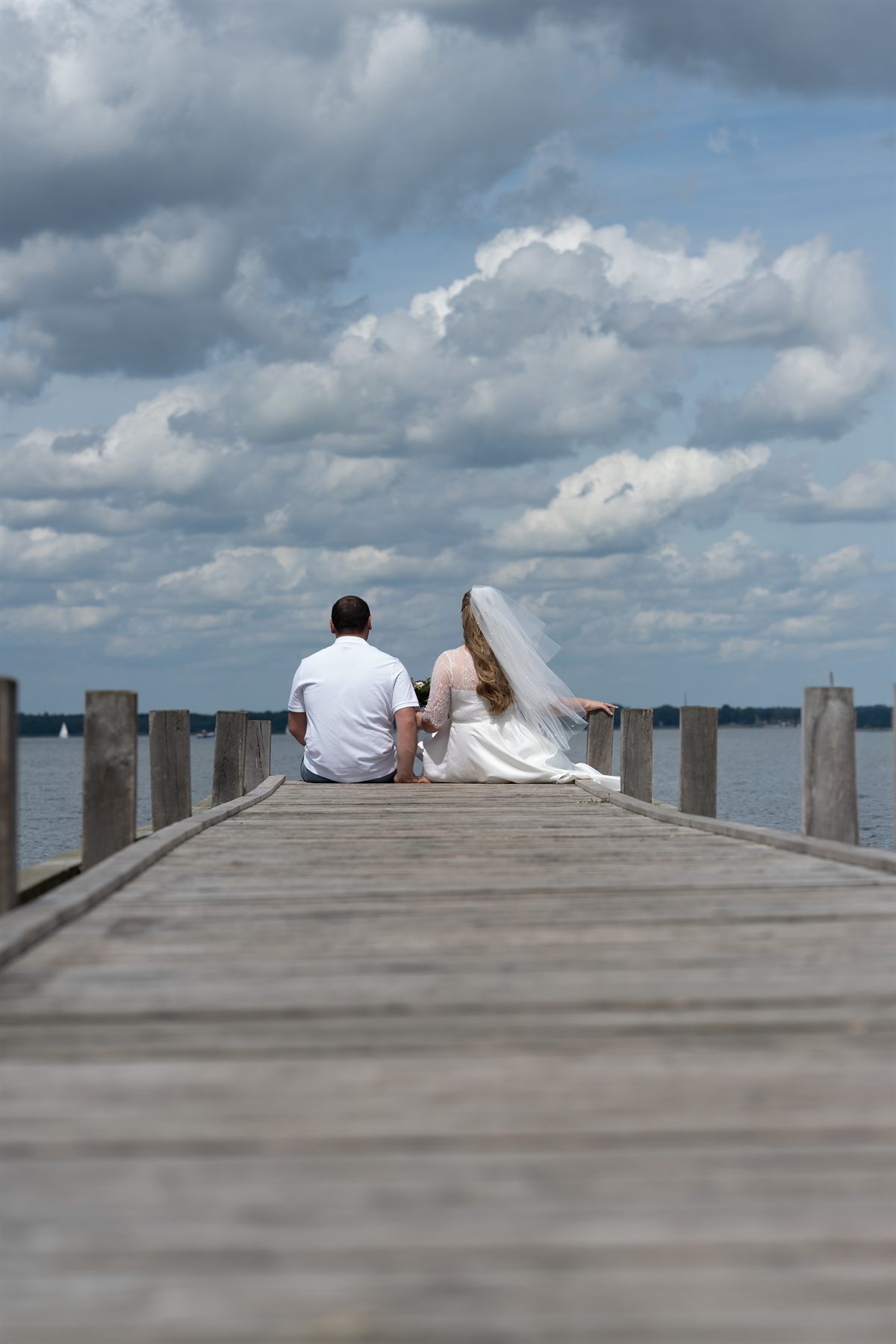 Newly-weds sitting at the end of a pier, looking out at the lake