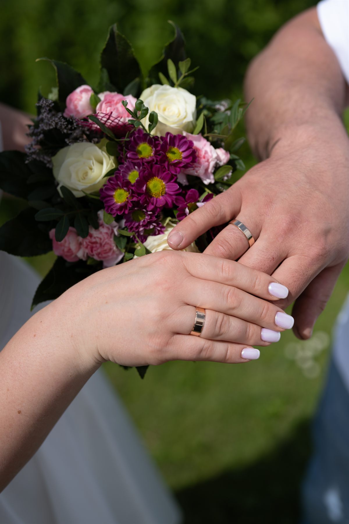 The couple's hands with their wedding rings, resting on the bouquet